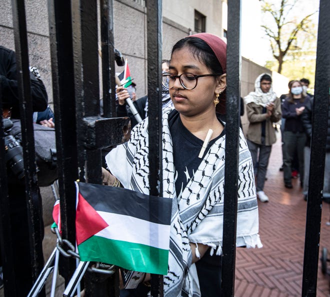 A Columbia University student places a Palestinian flag on an entrance gate to the campus in Manhattan April 22, 2024.