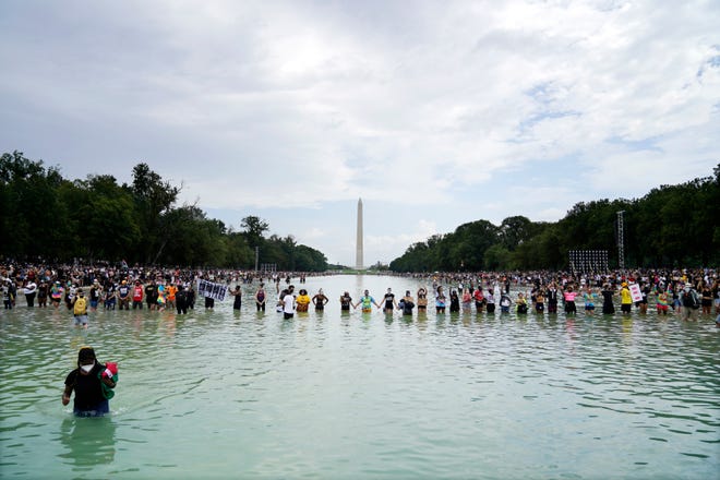 People pose for a photo in the Reflecting Pool in the shadow of the Washington Monument as they attend the March on Washington, Friday, Aug. 28, 2020, at the Lincoln Memorial in Washington, on the 57th anniversary of the Rev. Martin Luther King Jr.'s "I Have A Dream" speech.