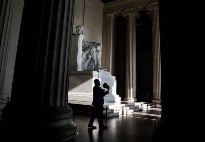 A man fans himself with his hat inside the Lincoln Memorial.